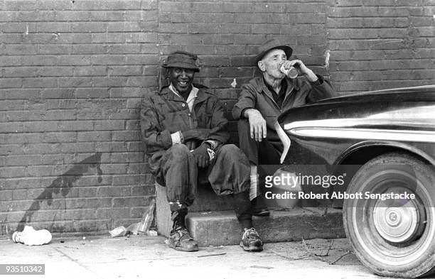Two elderly men, one of African American descent, sit and while away the day next to an automobile, Greenville, MS, 1971. The man on the right is...