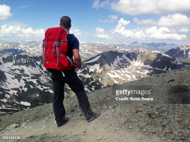 an adult male looks out over a mountain range alone on a remote mountain trail - robb reece stock-fotos und bilder