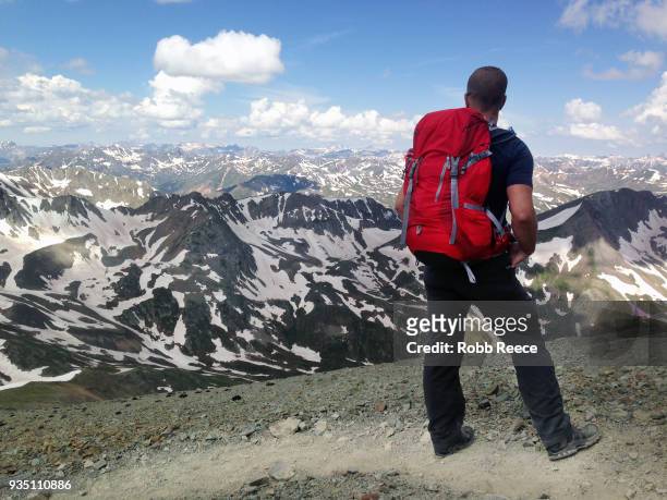 an adult male looks out over a mountain range alone on a remote mountain trail - robb reece stock-fotos und bilder