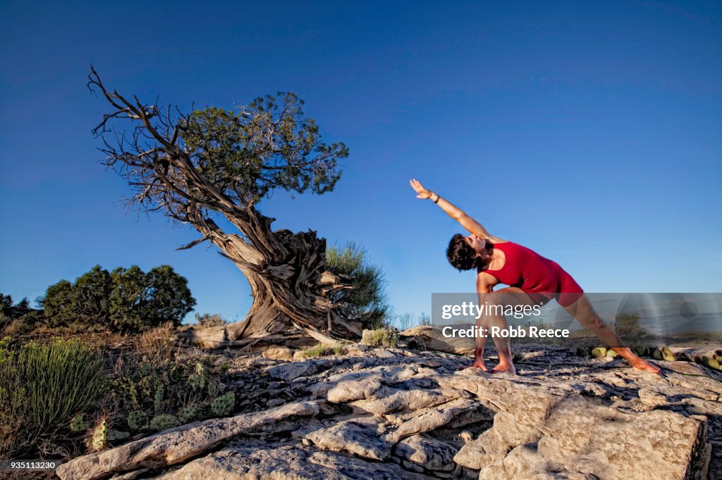 An adult woman practicing a yoga pose outdoors on a rock