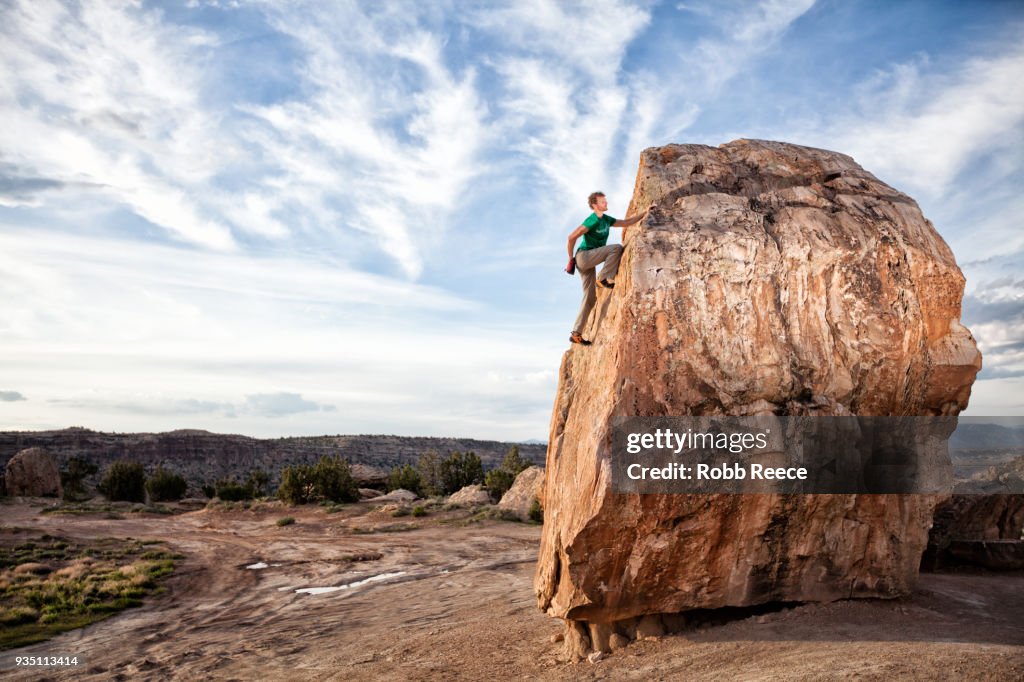 An adult man rock climbing on a rock in the desert