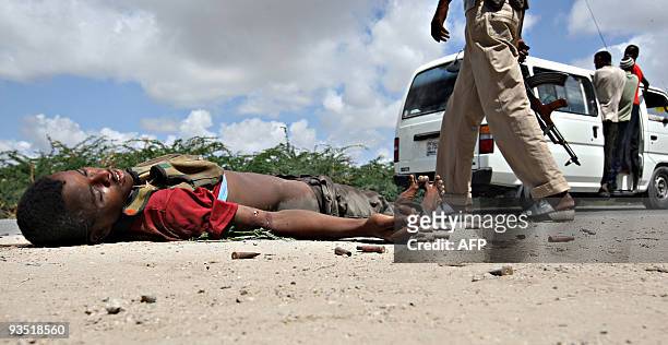 Government soldier walks past the body of a hard-line Islamic fighter and used ammunition shells at KM4 X-Control frontline section of Mogadishu...