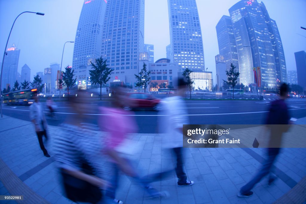 Pedestrians walking near building towers at dusk