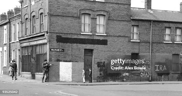 British army patrol moves past IRA graffiti on Ballyclare Street, in the Republican Ardoyne district of north Belfast, 19th April 1976. Such slogans...