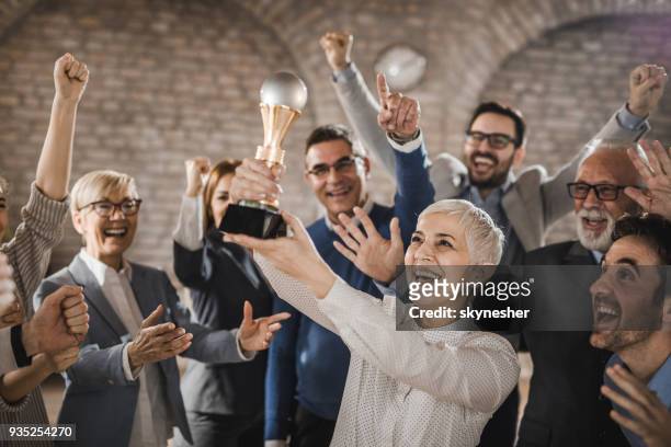 large group of joyful business colleagues celebrating their success by winning a trophy in the office. - awards inside stock pictures, royalty-free photos & images