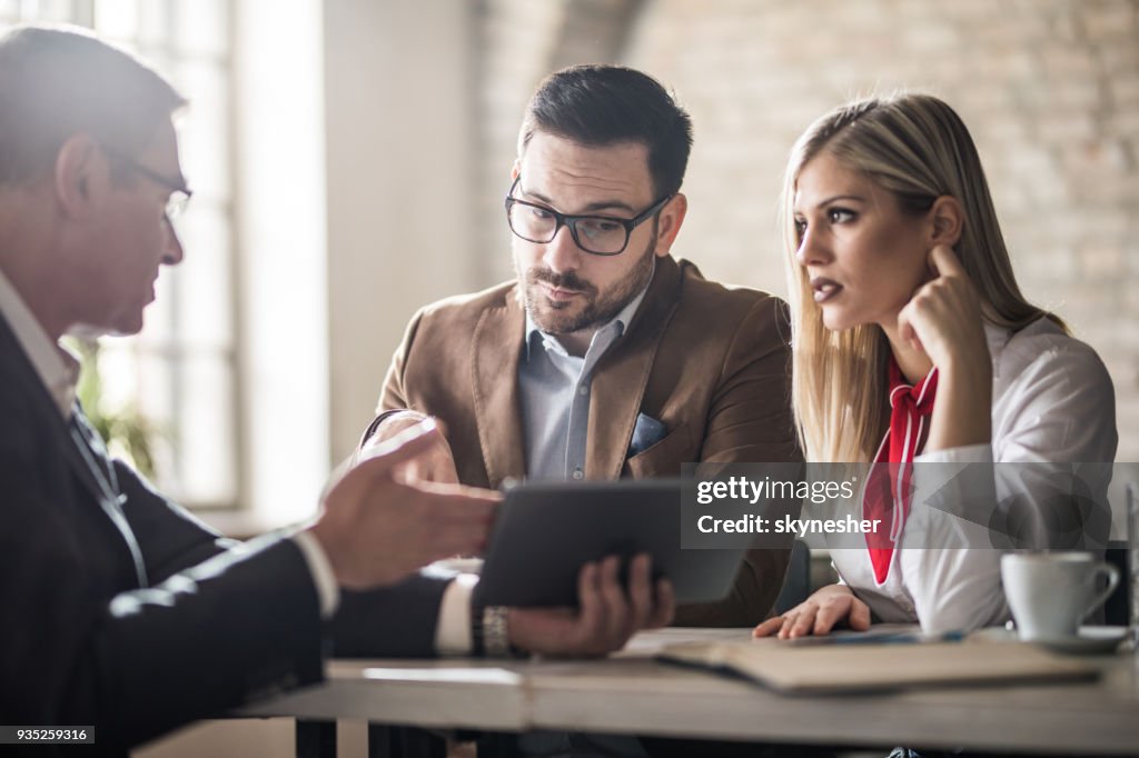 Young couple and their real estate agent looking at housing plan on touchpad in the office.