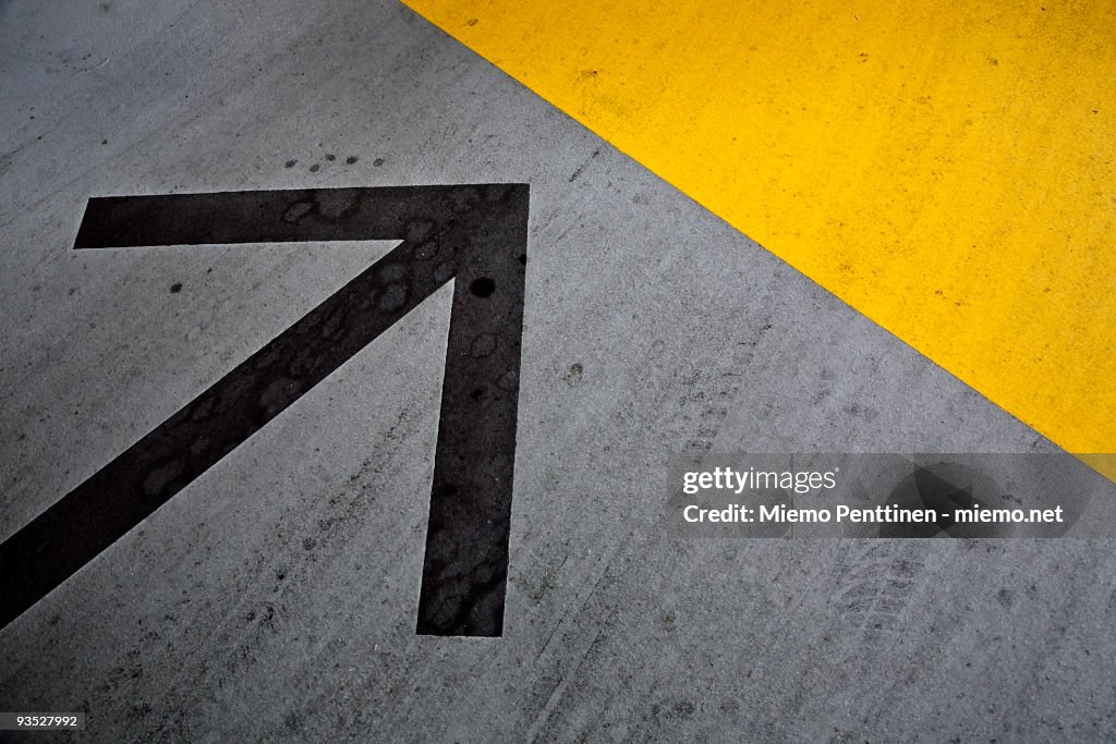 Arrow, a yellow wedge and tire marks on pavement
