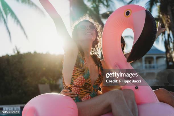 women friends with flamingo inflatable during swimming pool party - beach party stock pictures, royalty-free photos & images