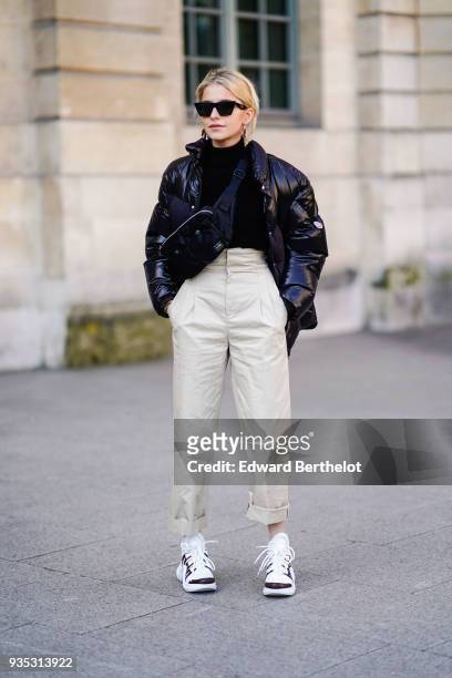 Caroline Daur wears sunglasses, a black turtleneck, a glossy black vinyl puffy jacket, off-white pleated waist cuffed pants, black and white...