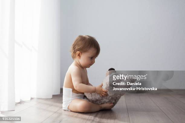 baby flicka sitter på golvet spelar med nalle - baby stuffed animal bildbanksfoton och bilder
