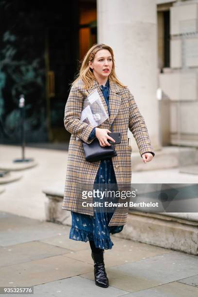 Guest wears a camel prince-of-wales checkered coat, a blue flowy dress with flounce at the end, a black handbag, black boots, during London Fashion...