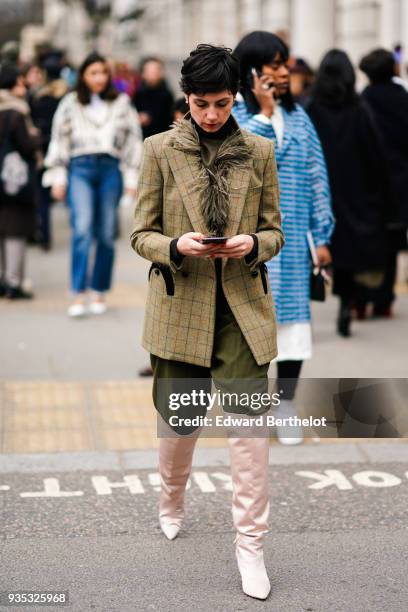 Guest wears a black turtleneck, a yellow-bronze fringe scarf, a yellow-bronze jacket, green pants, nacreous pale pink over-knee boots, during London...