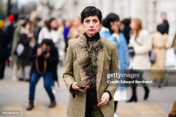 Guest wears a black turtleneck, a yellow-bronze fringe scarf, a yellow-bronze jacket, green pants, nacreous pale pink over-knee boots, during London...