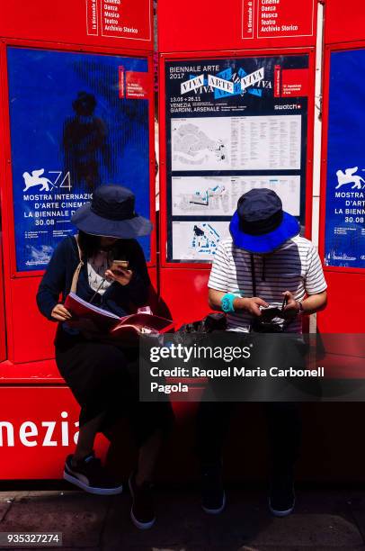 Japanese tourists sit in front of Venice film festival advertisement.