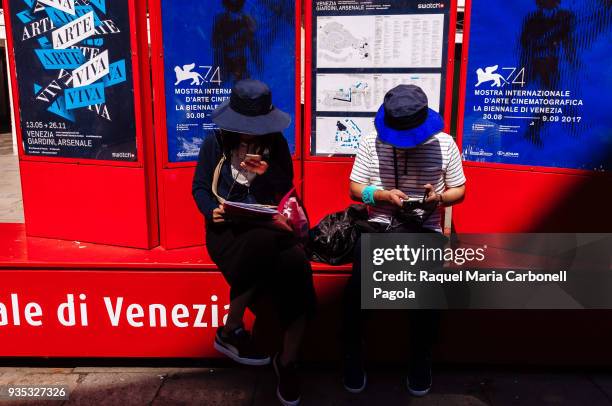 Japanese tourists sit in front of Venice film festival advertisement.