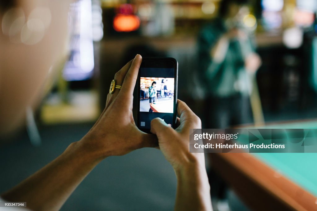 Woman Taking Photo Of Her Friend Playing Pool