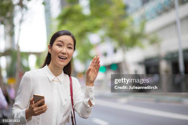 asian woman hailing a taxi in the city - australia taxi stock pictures, royalty-free photos & images