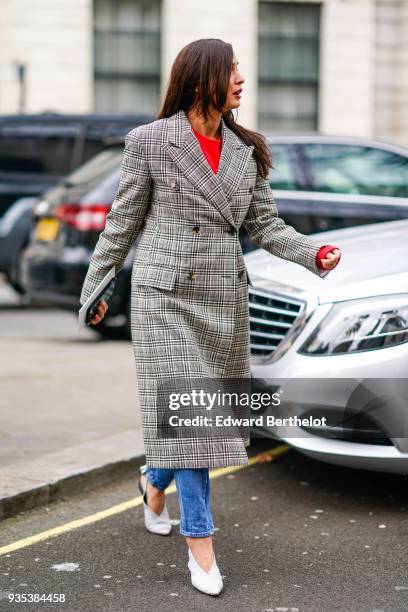 Guest wears a gray checked trench coat, a red top, blue jeans, white shoes, during London Fashion Week February 2018 on February 18, 2018 in London,...