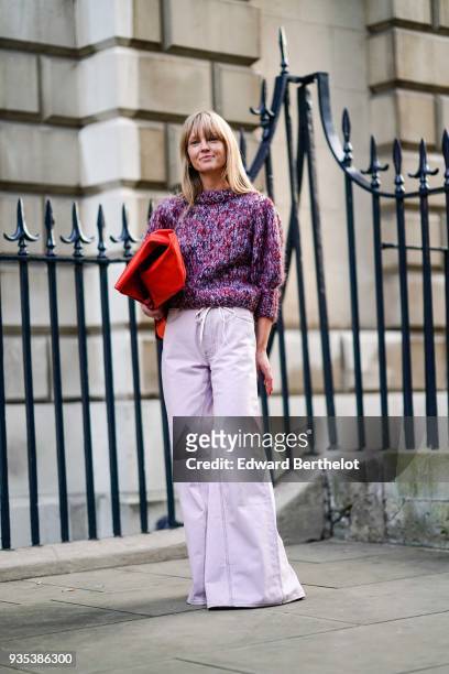 Guest wears a purple wool turtleneck pull over, purple flare pants, a red bag, during London Fashion Week February 2018 on February 16, 2018 in...