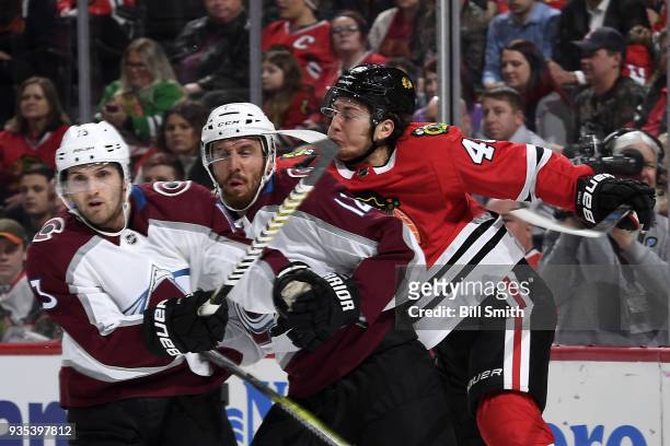 John Hayden of the Chicago Blackhawks gets physical with Alexander Kerfoot and Patrik Nemeth of the Colorado Avalanche in the first period at the...