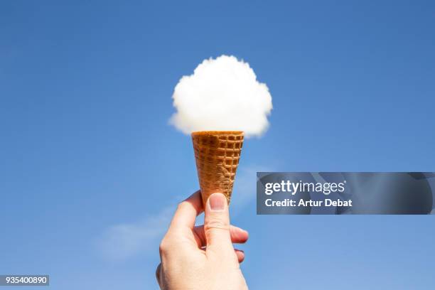 creative concept of a hand holding pov an ice cream cone with a cloud against a blue sky - ilusión óptica fotografías e imágenes de stock