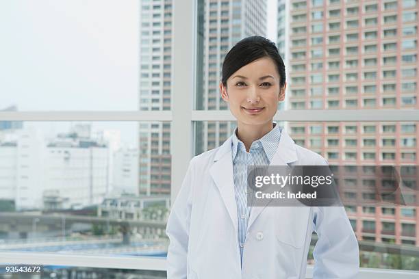 woman with white coat smiling by window - blouse blanche femme photos et images de collection