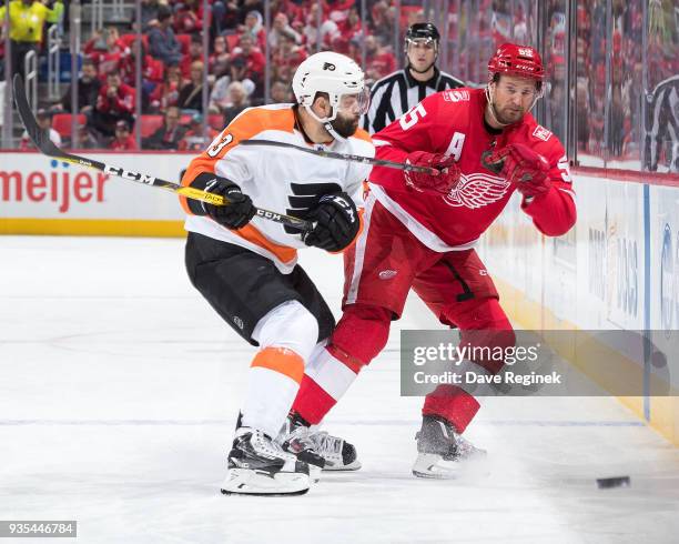 Niklas Kronwall of the Detroit Red Wings dumps the puck along the boards before getting checked by Radko Gudas of the Philadelphia Flyers during an...