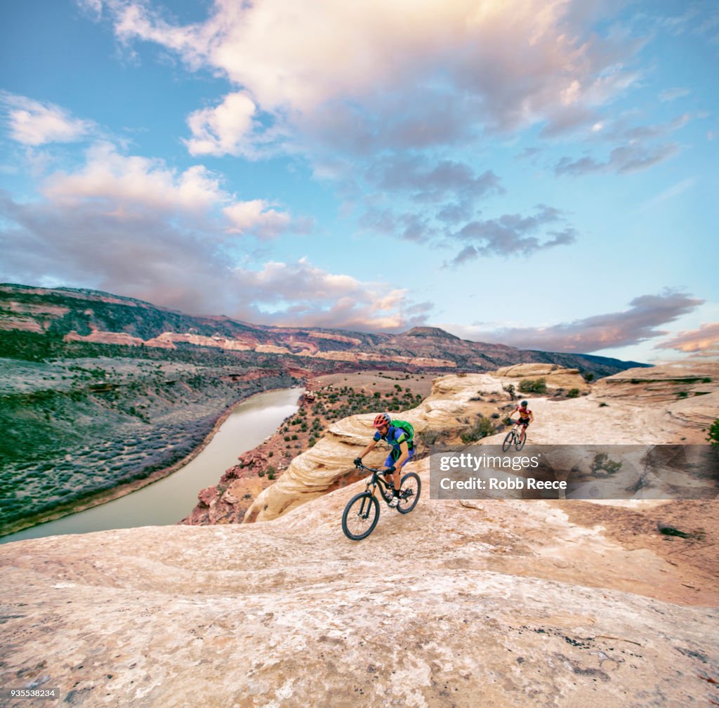 Two men riding a mountain bike on an extreme sandstone ledge
