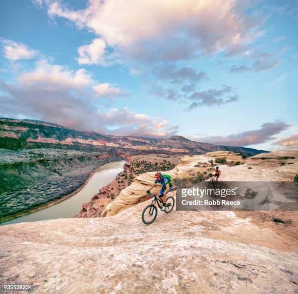 two men riding a mountain bike on an extreme sandstone ledge - robb reece stock pictures, royalty-free photos & images