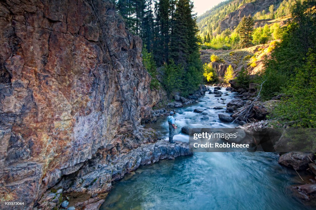 A male fly fisherman standing near a stream ready to fish