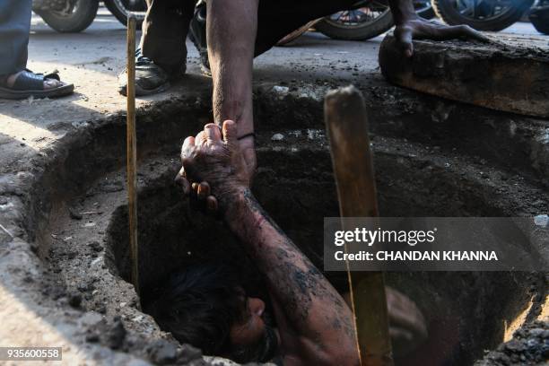 An Indian manual scavenger is helped out of a manhole in the old quarters of New Delhi on March 21, 2018. Slum dwellers depend on government supplies...