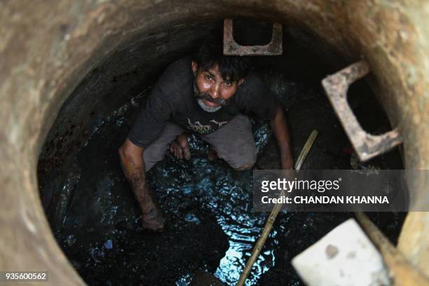 An Indian manual scavenger looks on as he cleans a manhole in the old quarters of New Delhi on March 21, 2018. Slum dwellers depend on government...