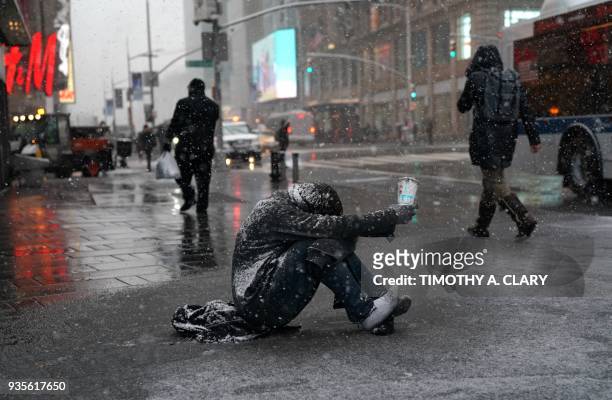 Man begs for money in the snow along 42nd Street in Times Square in New York on March 21 as the fourth nor'easter in a month hits the tri-state area...