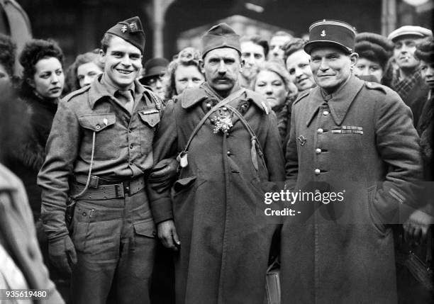 Un prisonnier de guerre rapatrié pose, brin de muguet à la boutonnière, entre deux militaires,dont un soldat de la France libre , devant la gare du...