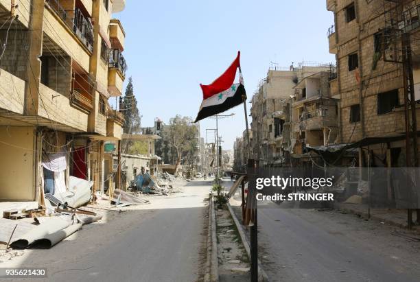 Syrian flag is seen flying on a damaged street in the Eastern Ghouta town of Kafr Batna on March 21 after pro-government forces took control of the...