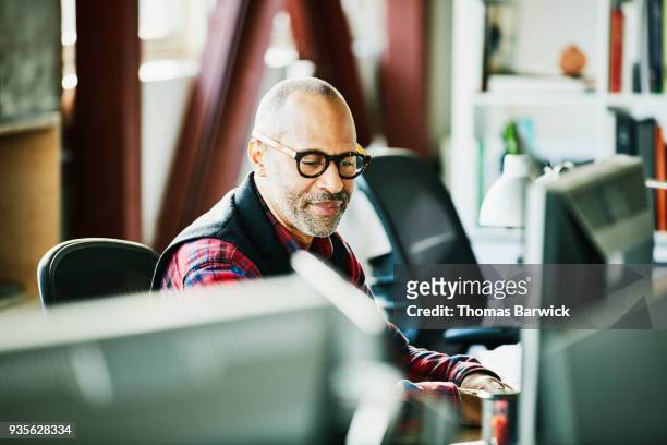 businessman looking at computer monitor at workstation in design office - abrigo negro fotografías e imágenes de stock