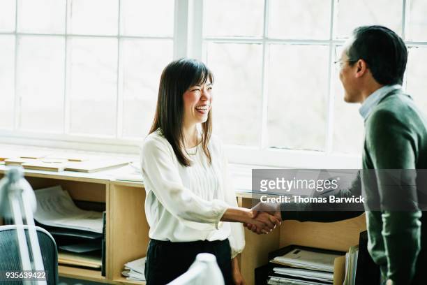 smiling businesswoman shaking hands with client in design studio - finance and economy stock pictures, royalty-free photos & images