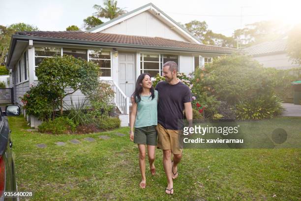happy mixed-race couple walking outside their front yard garden - suburban lifestyles stock pictures, royalty-free photos & images