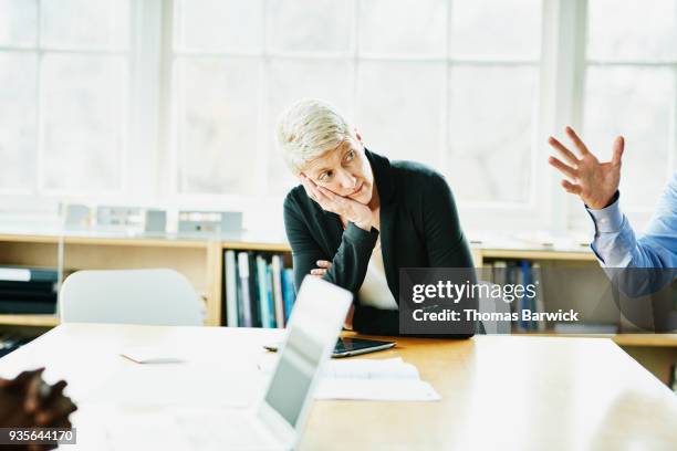 businesswoman with head on hand listening during meeting in office conference room - bored imagens e fotografias de stock