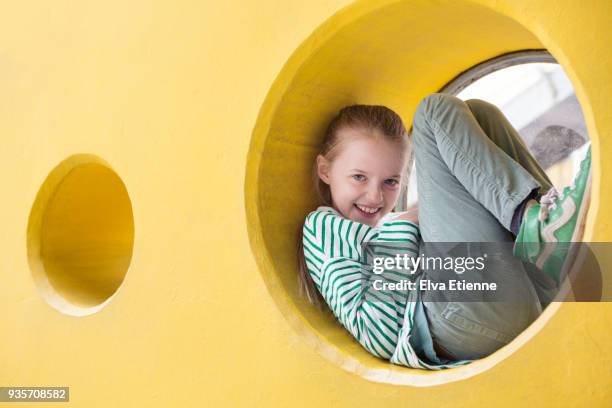 happy child (10-11) squashed into the frame of a circular window in a yellow wall - 10 11 jahre stock-fotos und bilder