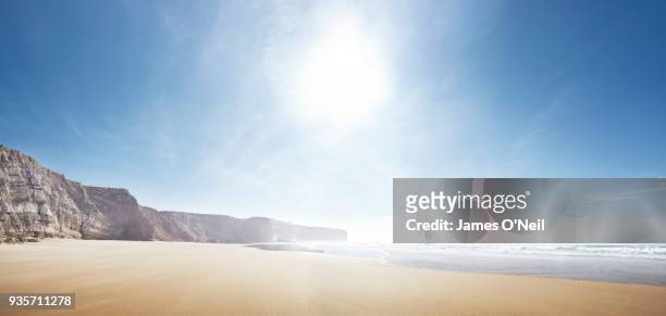 empty beach with sun and distant cliffs panoramic - sun beach stock-fotos und bilder