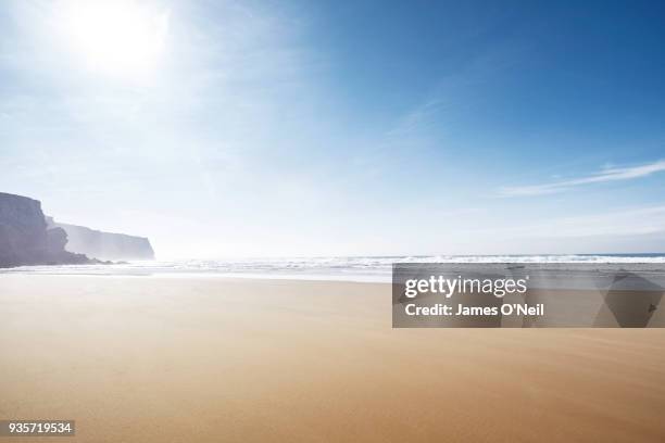 empty beach with sun and distant cliffs - portugal beach stock pictures, royalty-free photos & images