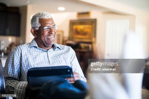entspannte senior schwarzer mann auf tablet in küche zu hause arbeiten - black men feet stock-fotos und bilder