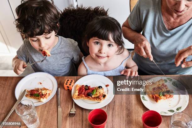 grandmother sitting at kitchen table with grandchildren, eating pizza, elevated view - comfort food stock pictures, royalty-free photos & images