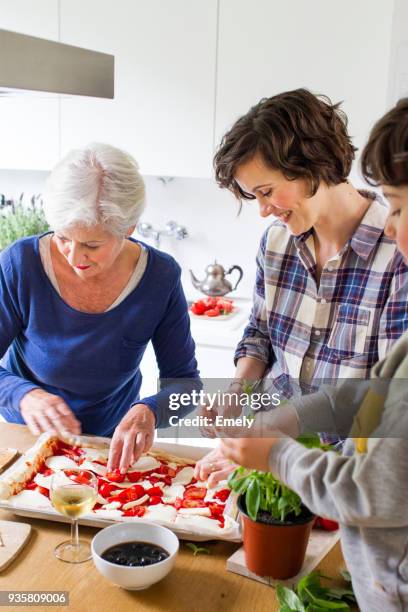 young boy, mother and grandmother making pizza together in kitchen - mujeres de mediana edad fotografías e imágenes de stock