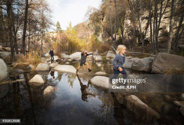 children playing on rocks in river, lake arrowhead, california, usa - stepping stones stockfoto's en -beelden