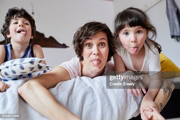 portrait of mother, son and daughter, lying on bed, poking tongue out - pull a face stock-fotos und bilder