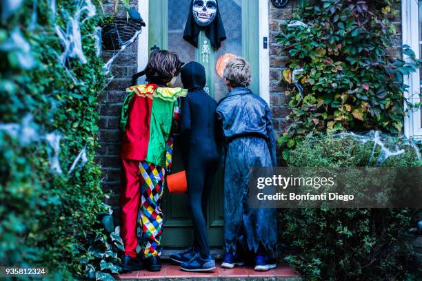 three boy in halloween costumes, standing at door, trick or treating, rear view - trick or treat stock pictures, royalty-free photos & images