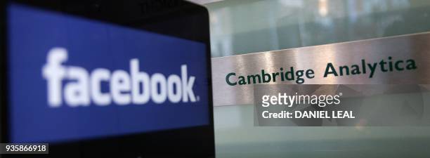 Laptop showing the Facebook logo is held alongside a Cambridge Analytica sign at the entrance to the building housing the offices of Cambridge...