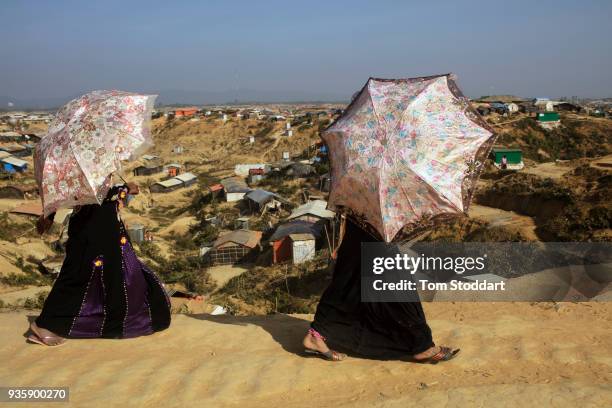 Two Rohingya women shelter from the sun under decorative umbrellas as they walk through Kutupalong refugee camp on February 27, 2018 at Cox's Bazar,...
